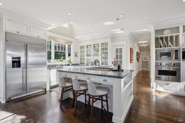 kitchen featuring a kitchen island, built in appliances, dark stone countertops, white cabinets, and open shelves