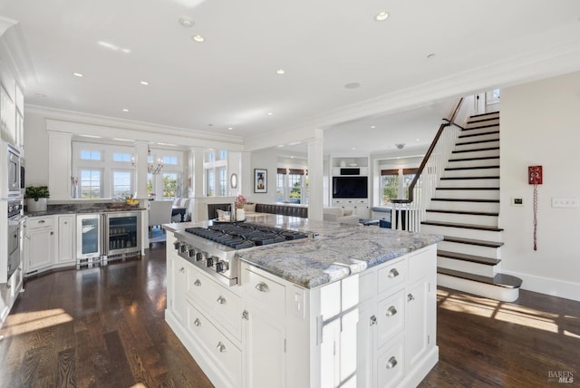 kitchen featuring light stone counters, beverage cooler, decorative columns, appliances with stainless steel finishes, and open floor plan