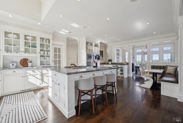 kitchen with a center island, glass insert cabinets, appliances with stainless steel finishes, a kitchen breakfast bar, and white cabinets