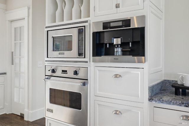 kitchen featuring stone countertops, stainless steel appliances, dark wood finished floors, and white cabinetry