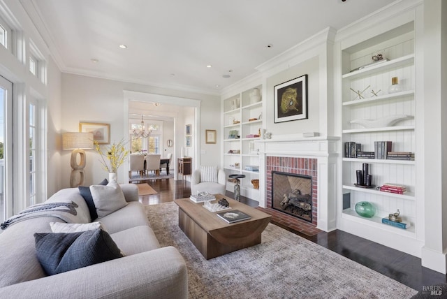 living room featuring a brick fireplace, crown molding, dark wood-type flooring, built in features, and a notable chandelier