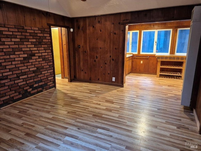 spare room featuring wood finished floors, wood walls, and brick wall