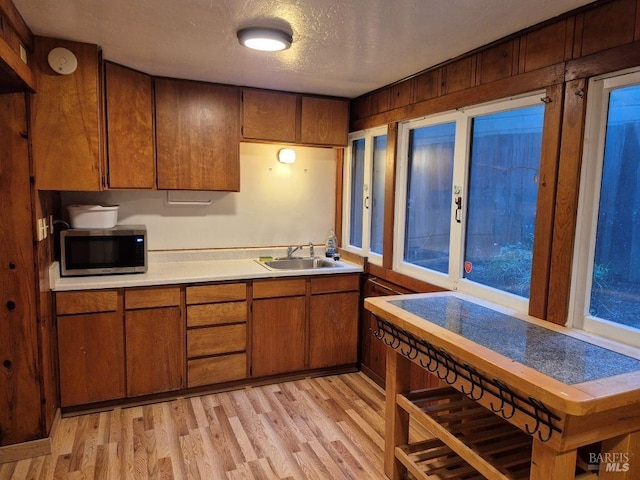 kitchen featuring stainless steel microwave, light countertops, brown cabinets, light wood-style floors, and a sink