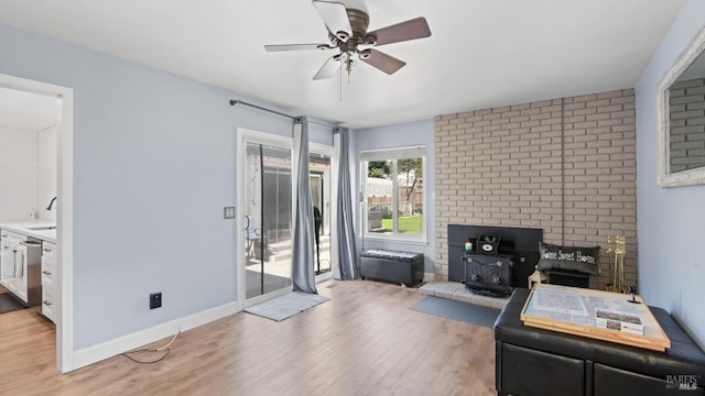 interior space with light wood-type flooring, a sink, baseboards, ceiling fan, and a wood stove