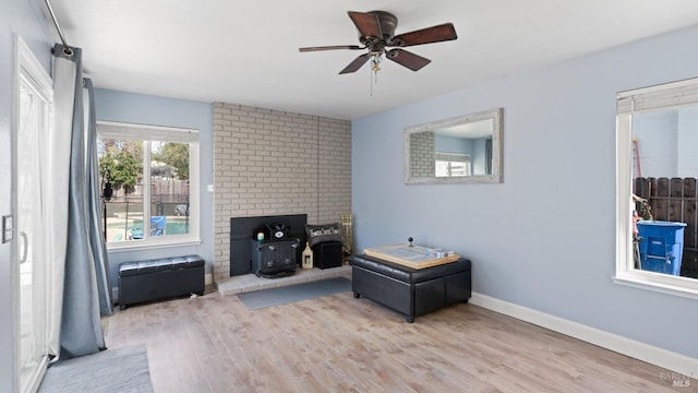 living area featuring a ceiling fan, a wood stove, baseboards, and wood finished floors