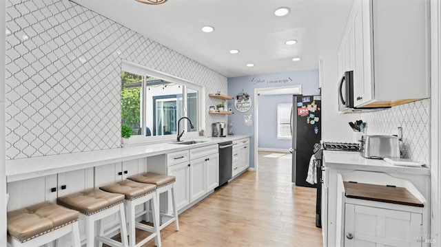 kitchen featuring white cabinets, a kitchen breakfast bar, backsplash, a sink, and appliances with stainless steel finishes