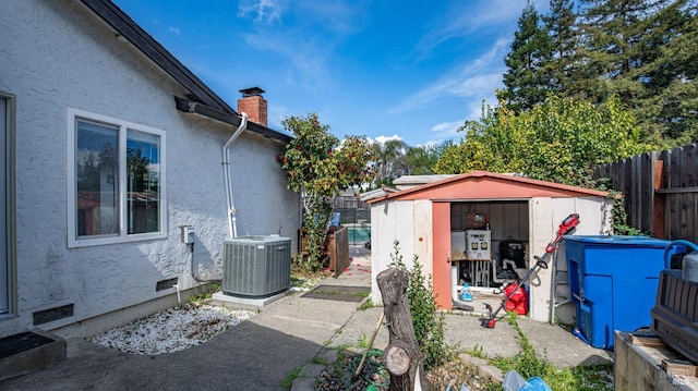 view of home's exterior featuring central AC unit, fence, a chimney, an outdoor structure, and a storage shed