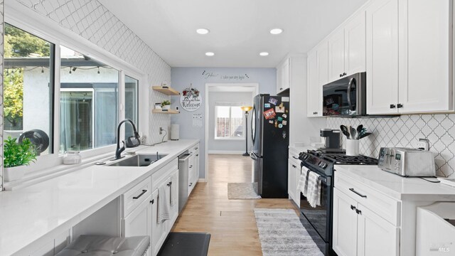 kitchen featuring light wood finished floors, a sink, white cabinets, stainless steel appliances, and open shelves