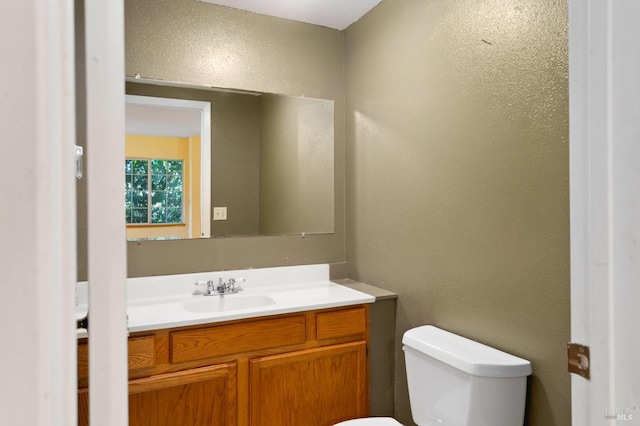 bathroom with a textured wall, toilet, and vanity