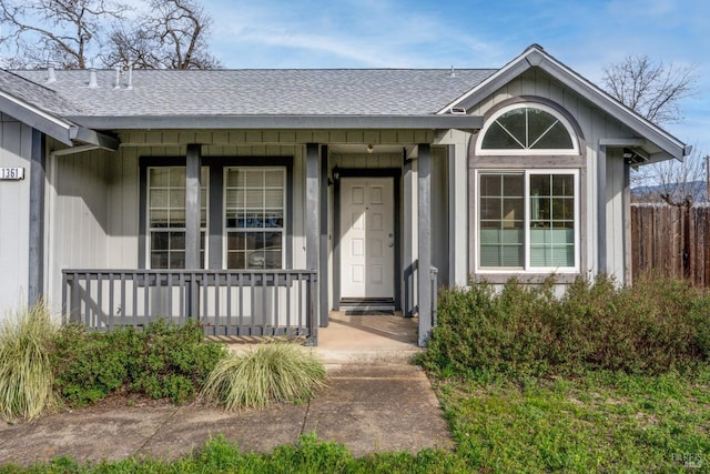 entrance to property featuring a porch, a shingled roof, and fence