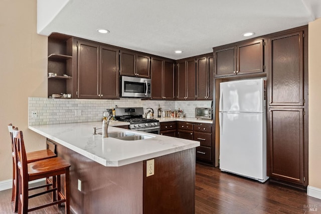 kitchen featuring open shelves, a peninsula, a sink, dark brown cabinetry, and appliances with stainless steel finishes