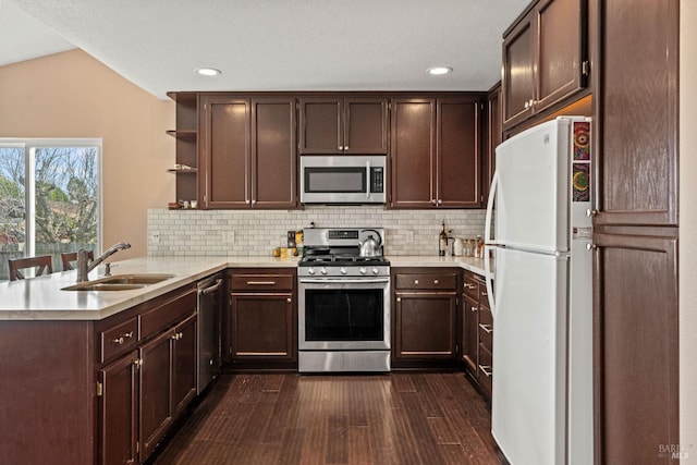 kitchen with dark wood-type flooring, a sink, backsplash, stainless steel appliances, and a peninsula