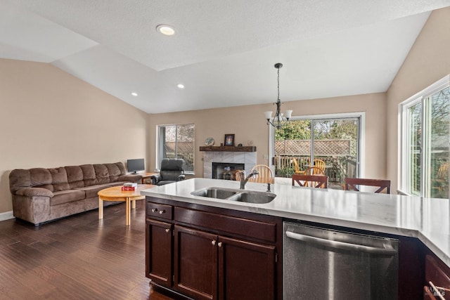 kitchen featuring dark wood-type flooring, vaulted ceiling, a tile fireplace, stainless steel dishwasher, and a sink