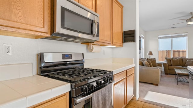 kitchen featuring open floor plan, appliances with stainless steel finishes, ceiling fan, and tile counters