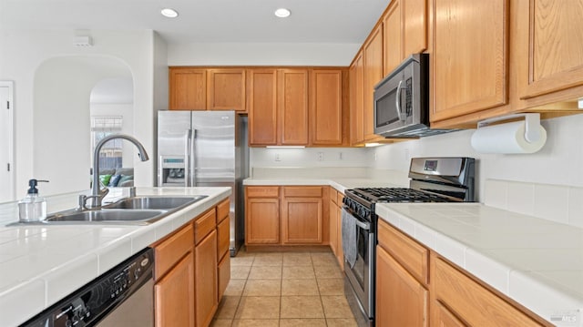 kitchen with light tile patterned floors, recessed lighting, a sink, stainless steel appliances, and tile counters