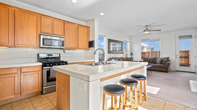 kitchen featuring an island with sink, a sink, open floor plan, tile countertops, and appliances with stainless steel finishes