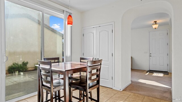 dining room with light tile patterned floors, baseboards, arched walkways, and light colored carpet