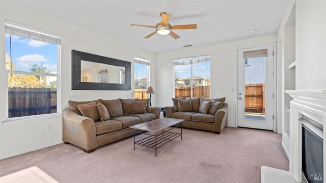 living area featuring visible vents, baseboards, light colored carpet, a fireplace, and a ceiling fan