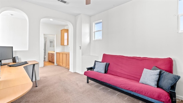 office space featuring baseboards, visible vents, arched walkways, ceiling fan, and light carpet