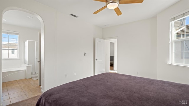 unfurnished bedroom featuring light tile patterned floors, visible vents, arched walkways, light carpet, and connected bathroom