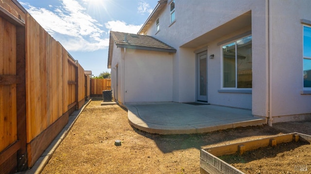 view of property exterior featuring a tile roof, central AC, stucco siding, a fenced backyard, and a patio