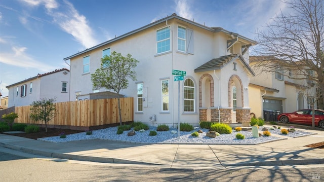 mediterranean / spanish house featuring fence, stone siding, and stucco siding