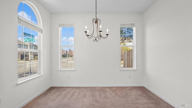 unfurnished dining area featuring baseboards, carpet, and an inviting chandelier