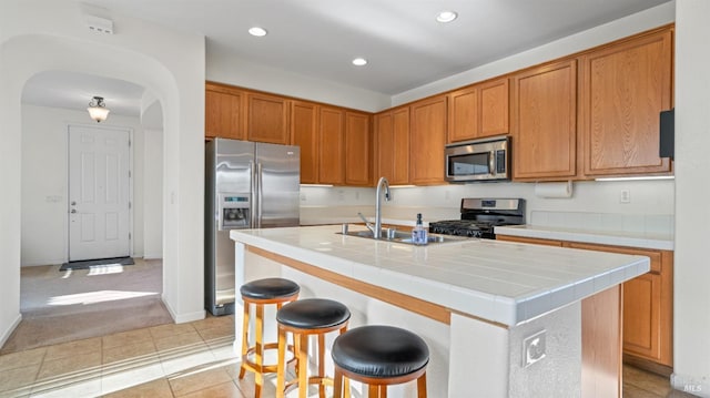 kitchen featuring tile countertops, recessed lighting, arched walkways, a sink, and appliances with stainless steel finishes