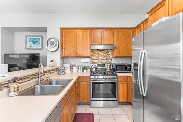 kitchen featuring under cabinet range hood, light countertops, brown cabinets, stainless steel appliances, and a sink