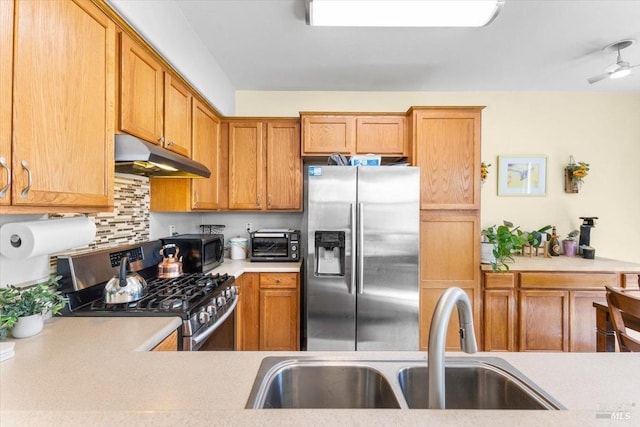 kitchen with a toaster, a sink, stainless steel appliances, light countertops, and under cabinet range hood