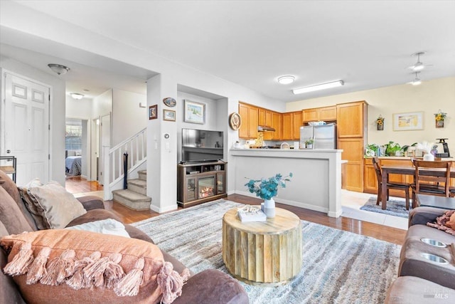 living area featuring stairway, light wood-style flooring, and baseboards