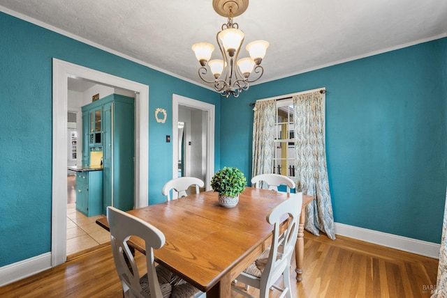 dining area featuring an inviting chandelier, wood finished floors, baseboards, and ornamental molding