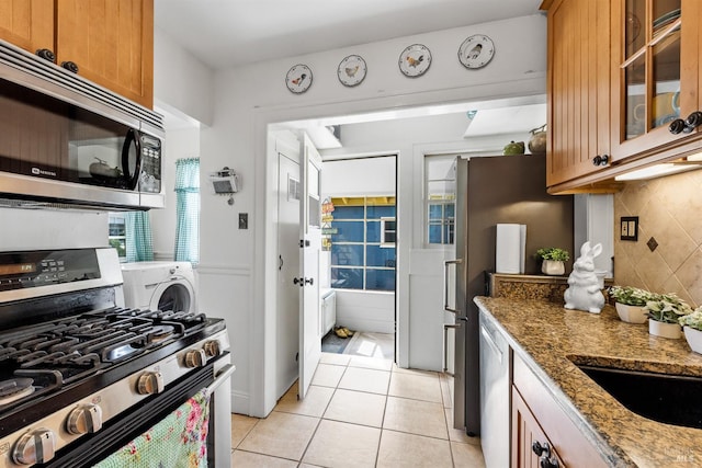 kitchen featuring light stone countertops, light tile patterned floors, decorative backsplash, brown cabinets, and appliances with stainless steel finishes