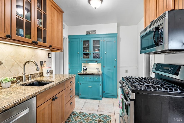 kitchen with light tile patterned floors, light stone countertops, a sink, stainless steel appliances, and tasteful backsplash