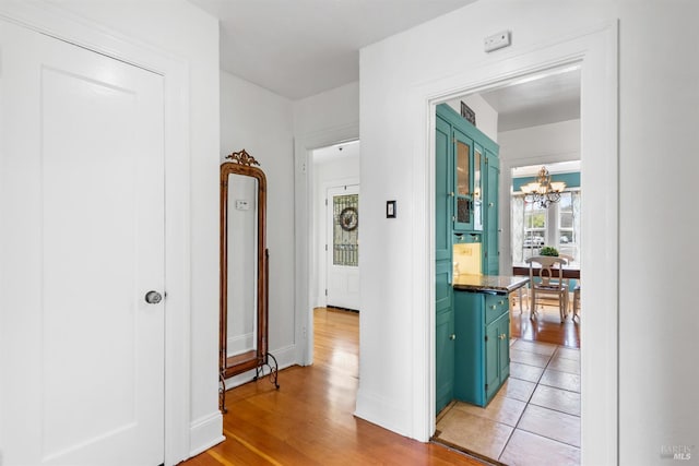 hall featuring a notable chandelier, light wood-style floors, and baseboards