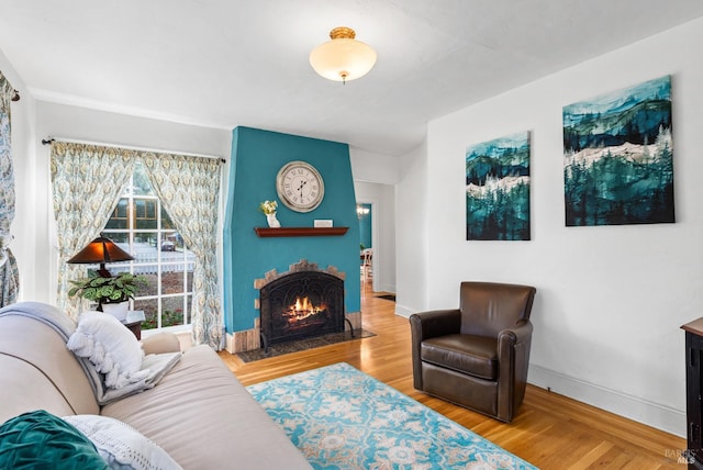 living room featuring a fireplace with flush hearth, baseboards, and wood finished floors