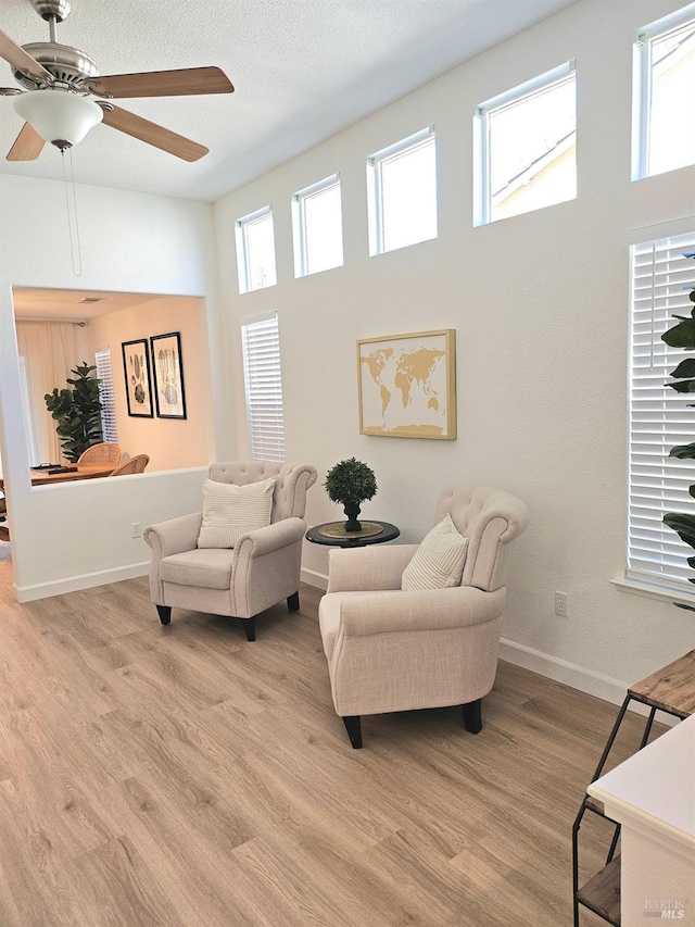 living area featuring baseboards, a high ceiling, light wood-type flooring, and a ceiling fan