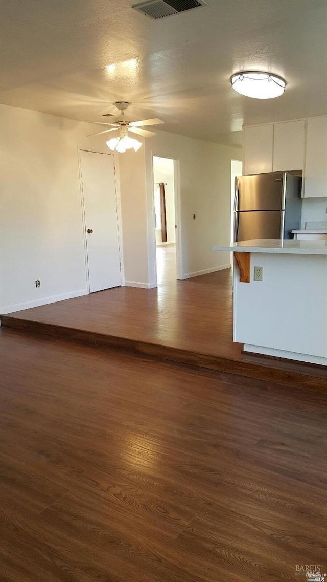 unfurnished living room featuring visible vents, baseboards, ceiling fan, a textured ceiling, and dark wood-style flooring