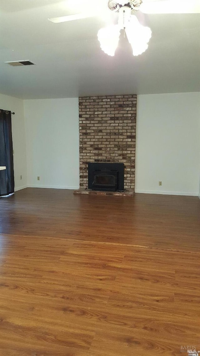 unfurnished living room with visible vents, a brick fireplace, and wood finished floors