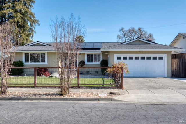 ranch-style house with a fenced front yard, concrete driveway, roof with shingles, roof mounted solar panels, and a garage