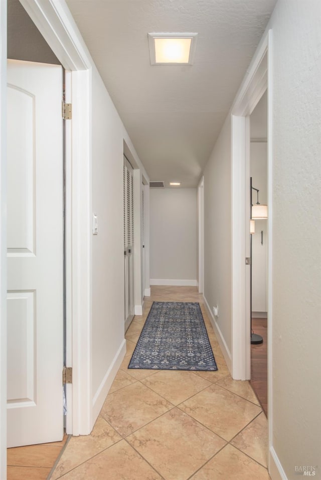 hallway with light tile patterned flooring and baseboards