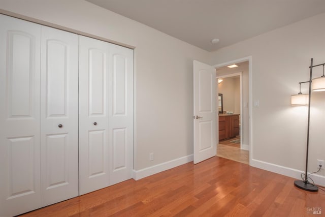 unfurnished bedroom featuring light wood-type flooring, baseboards, and a closet