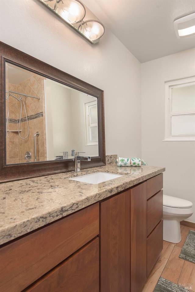 bathroom with tiled shower, toilet, wood finished floors, and vanity