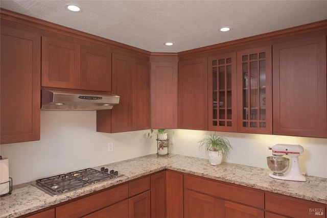 kitchen with light stone counters, recessed lighting, stainless steel gas stovetop, glass insert cabinets, and under cabinet range hood