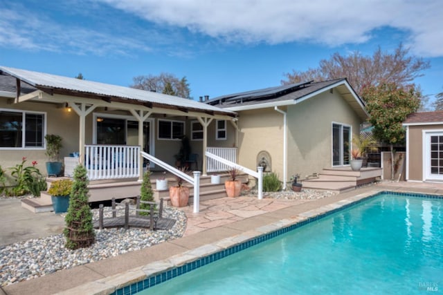 back of property with an outdoor pool, stucco siding, roof mounted solar panels, and a patio area