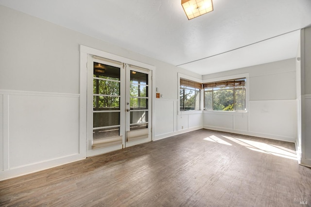 unfurnished room with a wealth of natural light, wainscoting, and wood finished floors