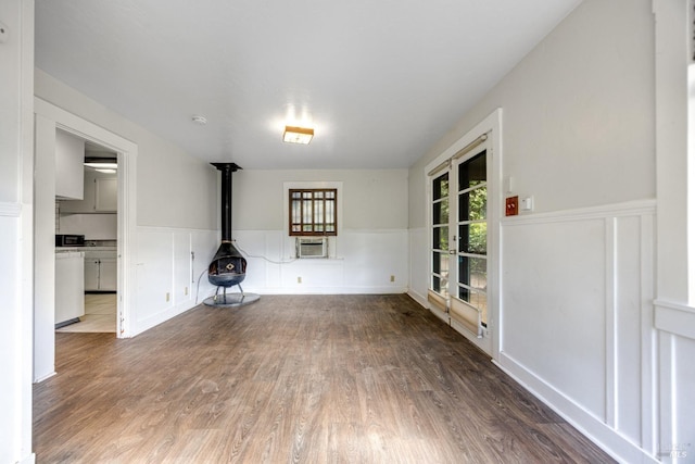 unfurnished living room with a wood stove, wood finished floors, and wainscoting