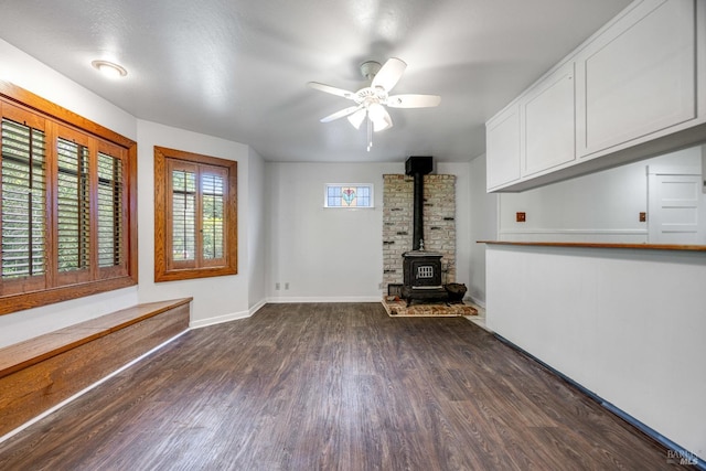 unfurnished living room with ceiling fan, baseboards, dark wood-style floors, and a wood stove