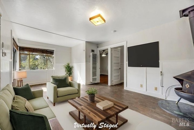 living room featuring a wainscoted wall, a wood stove, wood finished floors, and a ceiling fan