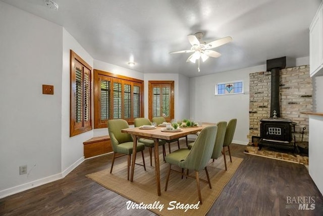 dining room with baseboards, a wood stove, ceiling fan, and wood finished floors